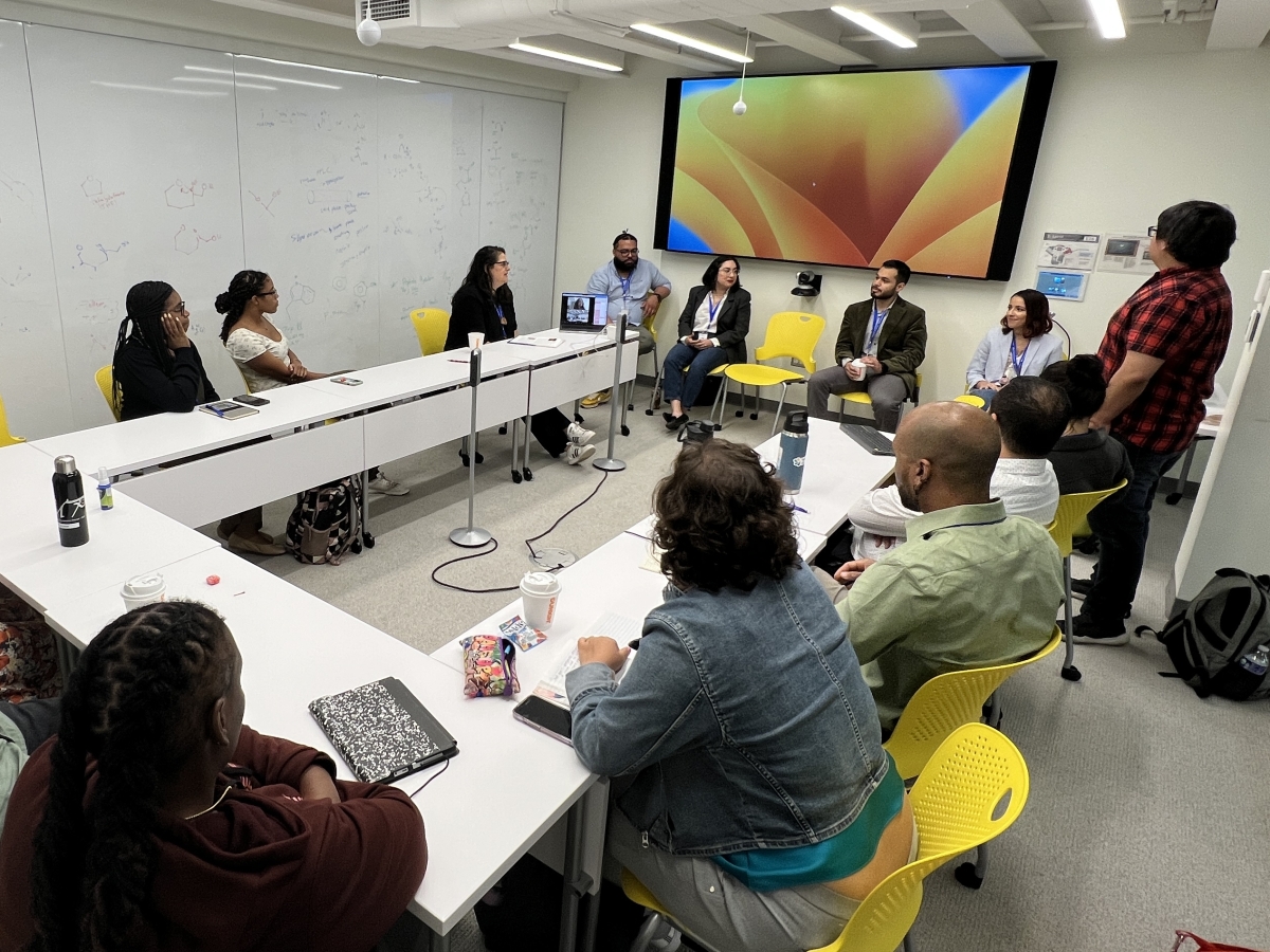 7 scientists seat u=in a U shaped table opposite a group of 4 panelists and 2 of the Yale Ciencia team memebers, listening to a talk.